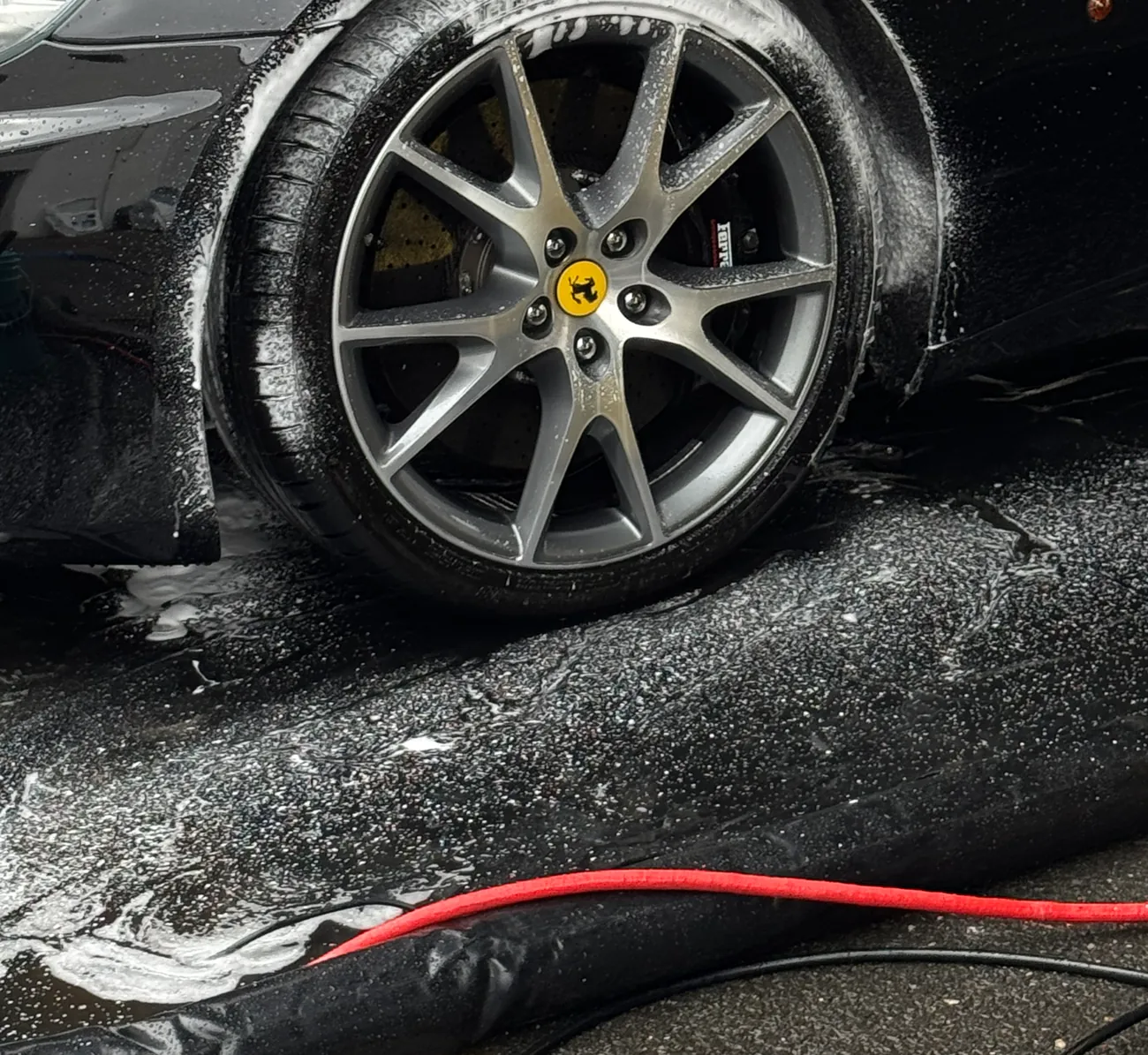 Jante d’une Ferrari noire en cours de lavage technique, tuyaux d’atelier au sol